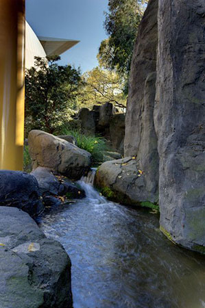 A miniature waterfall cascades into a body of water surrounded by large rocks.