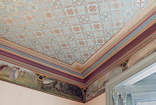 A corner view of Villa Alba’s dining room, with its painted frieze featuring scenes from Sir Walter Scott’s Rob Roy, and also showing a glimpse of the room’s intricate stencilled and hand painted ceiling