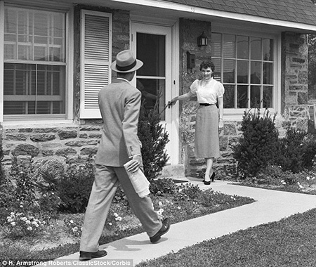 An immaculate housewife waits at the door to greet her husband