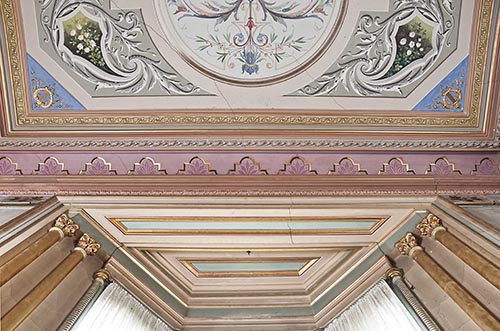 A detail of the drawing room at Villa Alba, showing the painted panelling and gold Corinthian capped pilasters surrounding the bay window, and the frieze and the ceiling’s art decoration