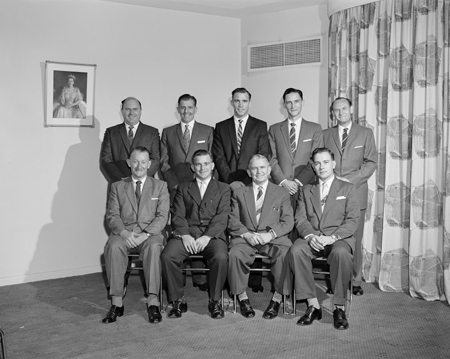 Staff photograph of postal inspectors with image of the Queen on the wall.